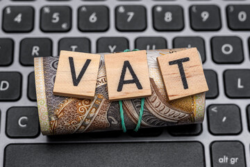 Napis VAT leży na papierowych pieniądzach na komputerze 