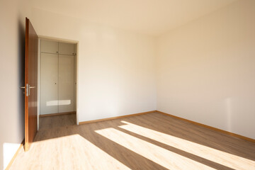 Fototapeta premium Empty room with white walls, an open door where you can see the hallway with built-in cabinets.