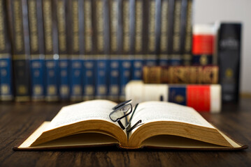 Open book and glasses on a wooden table and books in the background. World Book Day. Concept of reading.