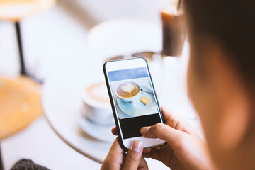 Woman photographing cup of latte on table in a cafe