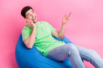 Photo of young cheerful man wear green t shirt jeans sitting bean bag has phone call look empty...