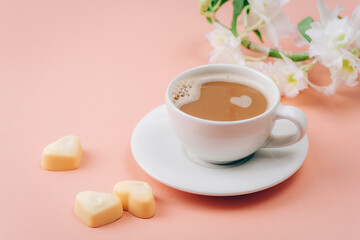 Coffee cup, heart shaped candies and white flowers on pink background. Valentines day concept. Closeup