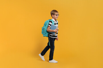 Fototapeta na wymiar Happy schoolboy in glasses with backpack and books on orange background