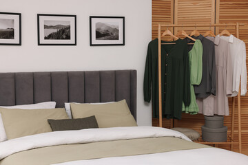 Comfortable bed and clothes on rack in stylish room