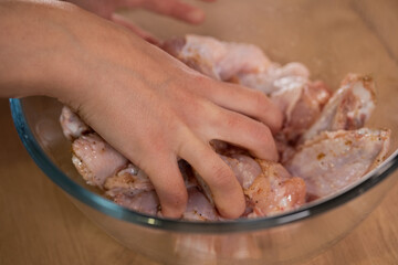 A hand mixes raw chicken wings with spices. Preparation of ingredients.