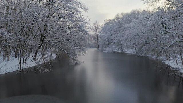 Flying through trees in winter snow landscape towards over frozen river