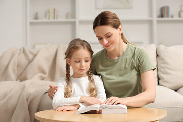 Girl and her godparent reading Bible together at table in room