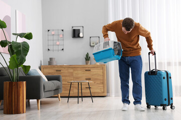 Travel with pet. Man holding carrier with cute cat and suitcase at home, space for text