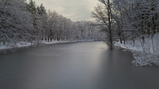 Flying through trees in winter snow landscape towards over frozen river