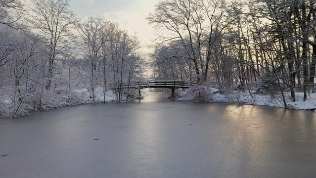 Flying under bridge and between trees in winter snow landscape over frozen river