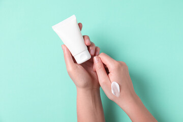 Woman with tube of hand cream on turquoise background, top view