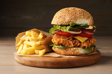 Delicious burger with crispy chicken patty and french fries on wooden table