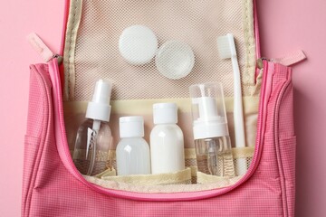 Compact toiletry bag with cosmetic travel kit on pink background, top view. Bath accessories - obrazy, fototapety, plakaty