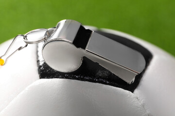 Football referee equipment. Soccer ball and metal whistle on green background, closeup