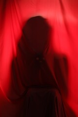 Silhouette of creepy ghost behind red cloth