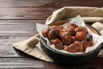 Roasted edible sweet chestnuts in bowl on wooden table, space for text