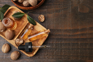 Nutmeg essential oil and nuts on wooden table, flat lay. Space for text