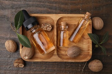 Obraz na płótnie Canvas Nutmeg essential oil and nuts on wooden table, flat lay