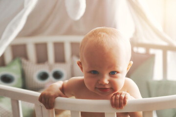 Portrait adorable baby with beauty blue eyes surprised in white round crib. Happy hairless little...