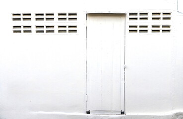 Painted white wood door closed on painted white cement wall and row of small channel beside both side, Thailand.