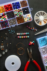 Colorful beads and various jewelry making supplies on dark background. Letter beads spelling JEWELRY MAKING. Top view.