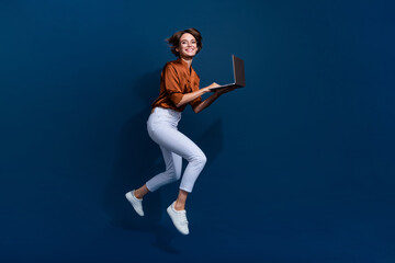 Fototapeta na wymiar Full length photo of pretty adorable lady wear brown shirt jumping communicating device empty space isolated blue color background