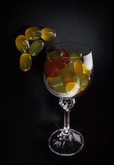A lot of candy canes are scattered from an overturned glass goblet. Multi-colored candies in a glass on a black background. Marmalade candies.