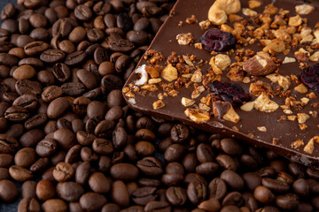 A bar of craft chocolate with various nuts, berries and dried fruits. Coffee beans. Food brown background