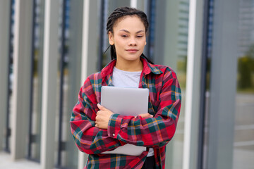 Portrait of an African-American female student with a laptop in her hands against the background of modern city buildings. The concept of education and training.