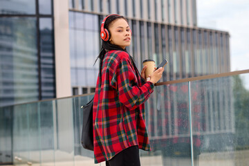 African-American woman navigates the city with headphones and her cherished coffee.