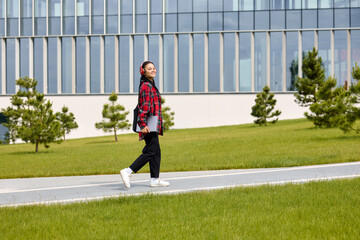 Obraz premium A general plan of a young woman walking along a path in the park with a laptop. Freelance, digital marketing, startup.