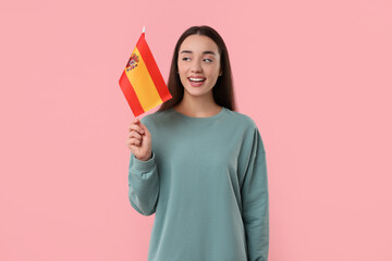 Young woman holding flag of Spain on pink background