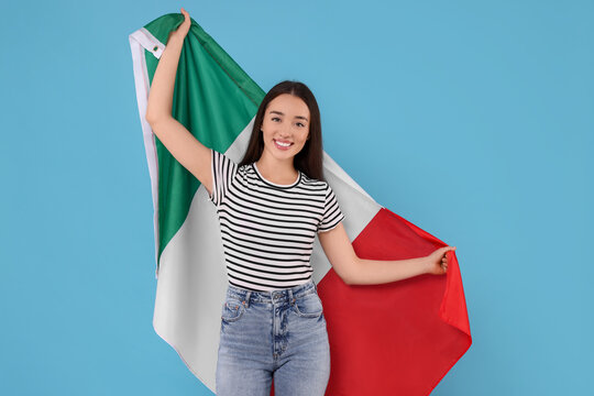Young woman holding flag of Italy on light blue background