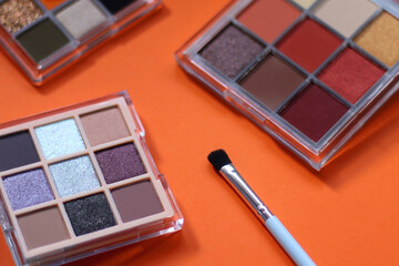 Colorful eyeshadow palettes and make up brush on orange background. Selective focus.
