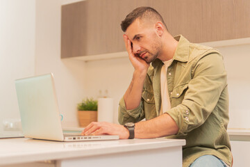Young adult man in front of the laptop looking worried, exhausted and anxious for the paperwork. Person upset and looking serious working on the computer and handling the stress