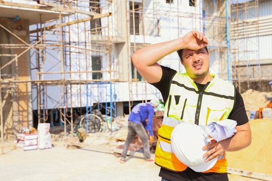 Foreman working outdoors condominium construction project exhausted from the hot weather and thirsty tired dizzy headache is dehydrated and wants to drink water suffer dehydration heatstroke.
