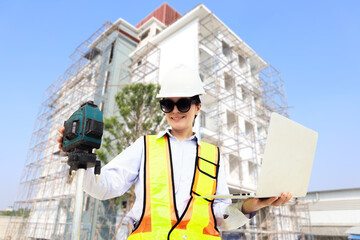 Female engineer foreman holds laptop computer setup and checks  modern technology tools laser level and vertical marker (Plum Bob) on tripod at construction site, condominium building.