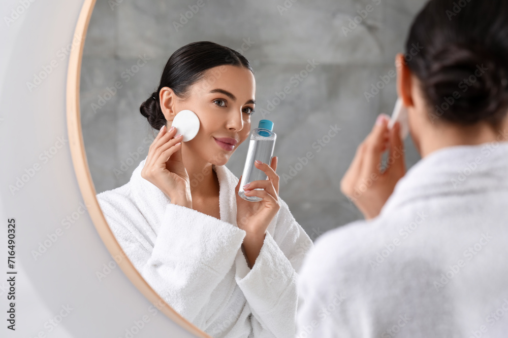 Wall mural beautiful woman removing makeup with cotton pad near mirror indoors