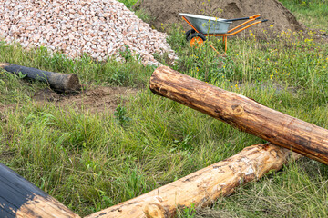 Preparation for construction works. New development area for summer houses. Wooden logs, Two-wheeled wheelbarrow with metal carcass, crushed rock, sand.
