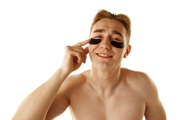Young shirtless man taking care after skim, applying under eye moisturizing patches isolated over white background. Refreshment. Concept of male beauty, skin care, cosmetology and cosmetics, health