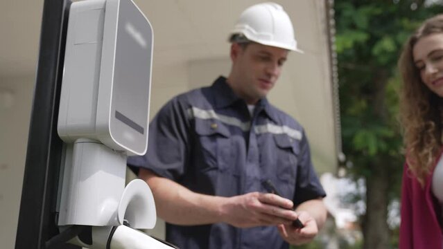 Technician install home EV charging station, providing service support for EV app on customer smartphone for monitoring charging status and set charging schedules at home. Fastidious
