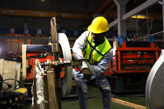 Black african american male worker works roof sheet metal rolling machine at high speed when accident suddenly causes his arm to get locked into the steering wheel causing his arm to break in pain.