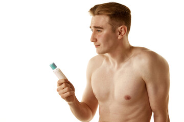 Fototapeta premium Shirtless handsome young guy holding face moisturizing cream jar isolated over white background. Morning spa. Concept of male beauty, skin care, cosmetology and cosmetics, health