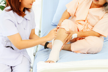 Fototapeta premium Female nurse care elderly female patient hospitalized patient with ankle pain from sprained foot Nurse uses bandage relieve pain makes patients feel good and encourages them to recover from illness.