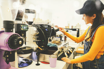 Beautiful asian female barista dressed bright yellow lifestyle outfit runs coffee shop selling food and drinks in the morning standing at the counter taking orders for espresso coffee modern machine.
