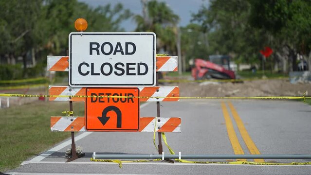 Warning roadworks sign and safety barrier on city street during maintenance repair work.