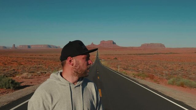 Close-up shot of young adultman looking around on highway, walking away at epic cinematic sunny sandstone desert in USA