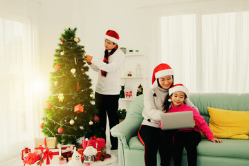 Happy family holding a Christmas party in their home : Decorate the christmas tree with beautiful gifts as father and mother and daughter sit on the sofa and relax comfortably.