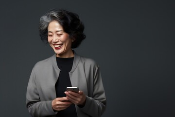 Smiling mature asian american woman with a smartphone isolated on a grey background