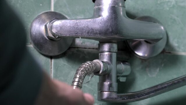 Man's hand holds damaged leaking water faucet hose in bathroom of house, apartment or other place. Plumbing concept. Malfunction of bathroom and faucet in shower. Plumber call.